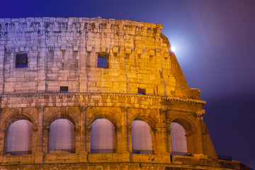 Dettaglio del Colosseo di notte con la luna piena in lunga esposizione  e finestre infuocate