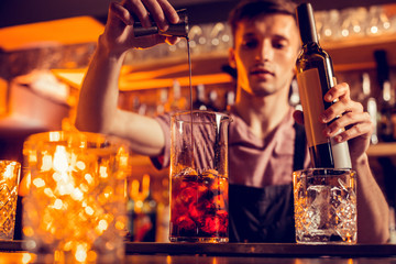 Handsome young barman pouring alcohol into cocktail