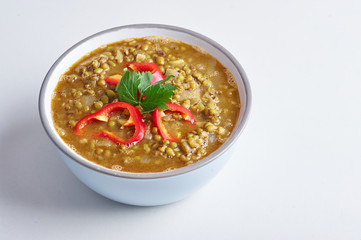 Mung Dhal with red pepper slices isolated at white. Moong Dal - Indian Cuisine curry. Vegetarian dish with mung beans, zira cumin, coriander and chili