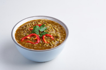 Mung Dhal with red pepper slices isolated at white. Moong Dal - Indian Cuisine curry. Vegetarian dish with mung beans, zira cumin, coriander and chili