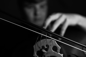 A young cellist practices intensely on his cello, viewed from the bridge and bow side © James