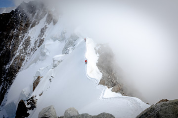 Two alpinists walking thin mountain ridge.