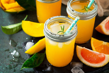 Refreshing summer cocktails made of citrus and mango, cold drink with ice on a dark stone background. Concept fresh vitamins. Rustic style.