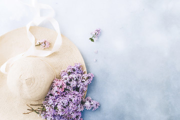 Women`s summer hat with a ribbon and a bouquet of lilac flowers on a blue background. Top view. Flat lay.