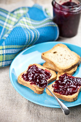 Toasted cereal bread slices on blue ceramic plate and homemade wild berries jam in jar, spoon and linen napkin.