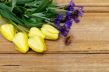 Overhead view of yellow tulips and blue cornflowers on wood background with copy space. Tulips close up. Easter card with space for your greetings.