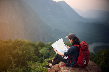 Backpacker woman sitting on top of mountain and looking map with nature background
