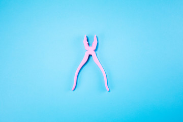 Pink pliers lie on pastel blue background. Minimal summer concept.