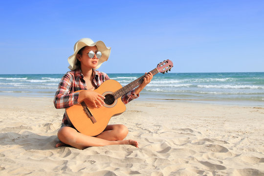 Asian beautiful girl wearing plaid shirt playing guitar on a beautiful beach