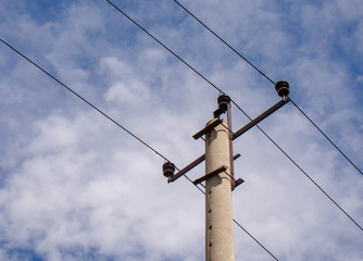 Electric concrete pole with wires. Background sky with light clouds. Metal constructions. Ceramic insulators.