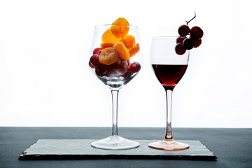 Dried apricots and grape berries in glass and portion of red wine on white background
