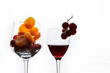 Dried apricots and grape berries in glass and glass of red wine on white background