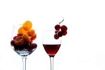 Dried apricots and grape berries in glass and glass of red wine on white background