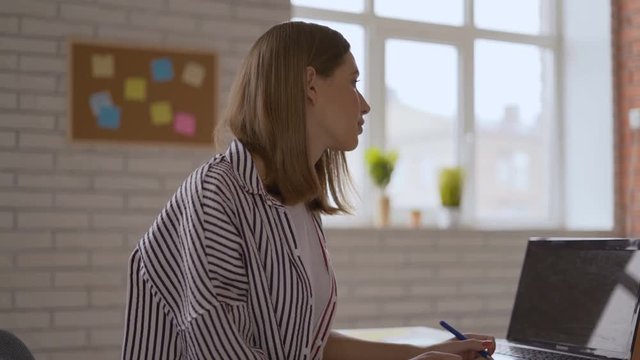 Cute attractive schoolgirl attentively listens to the teacher and writes with her left hand. 4K