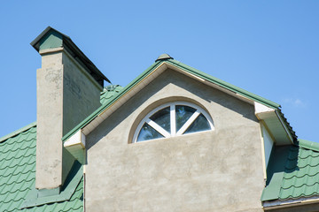 Close-up of building, attic rooms exterior on metal shingle roof, stucco walls and plastic windows.