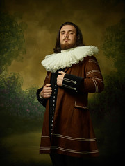 Young man as a medieval knight on dark studio background. Portrait in low key of male model in...