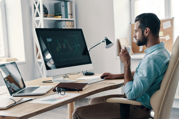 Working day. Young modern businessman analyzing data using computer while sitting in the office