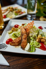 Caesar salad with fried fish on an original square white plate in table setting setup - closeup photography
