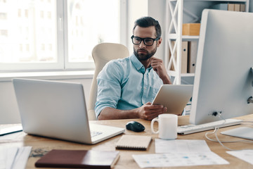 Innovation. Young modern businessman working using digital tablet while sitting in the office