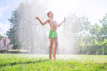 Cute  preschooler boy refresh herself from garden watering hose on the family country house grass...