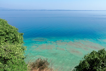 Beautiful emerald and calm waters of Lake Garda near Sirmione town, Italy. On the horizon in the fog the shore with small towns on the lake.