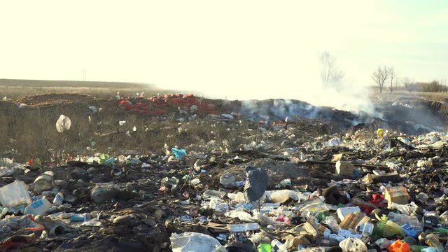Large garbage dump waste with smoke at sunny day