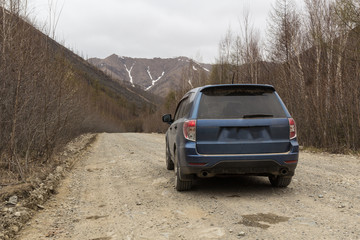 Off-road car, standing on a gravel road in the woods and mountains. In the distance you can see snowy peaks.