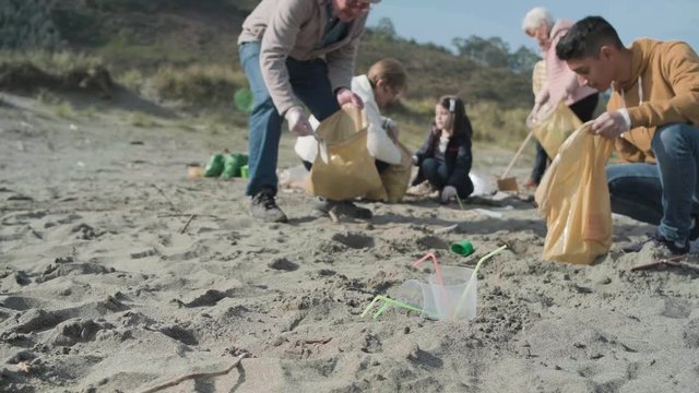 Plastic cups and straws on the beach with group of volunteers cleaning in the background. Selective focus in foreground