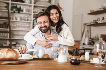 Portrait of joyful european couple eating at table while having breakfast in kitchen at home