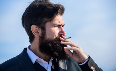 Bearded hipster smoking cigarette blue sky background. Guy enjoy cigarette. Man beard and mustache...