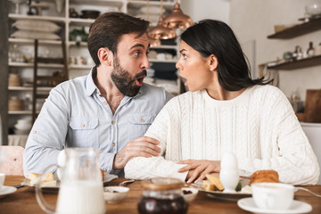 Portrait of excited couple eating together at table while having breakfast in kitchen at home