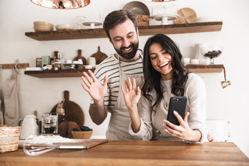 Portrait of caucasian couple hugging together and holding smartphone while cooking in kitchen at home