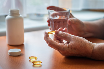 Senior woman is holding omega-3 food supplement capsule in hand