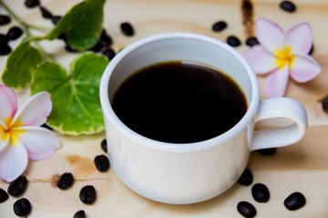 Black coffee cup with a pink frangipani flowers And green leaves And coffee beans are in the composition