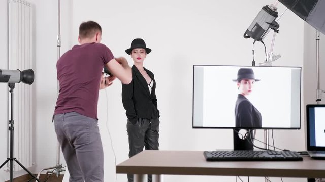 Professional model wearing a hat and photographer taking pictures of her in studio with flashes and other lighting equipment