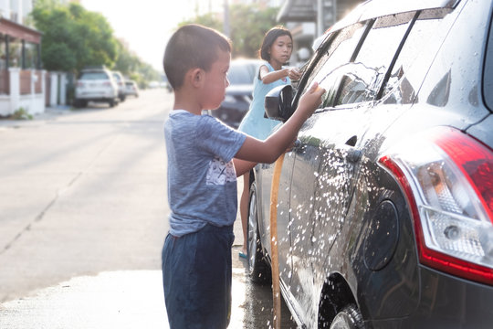 Asian children are using water hose to washing car in the mornign, cute kide are helping to wash their car with fun at the front ot the house.