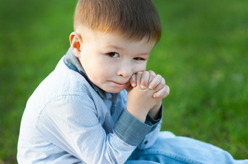 Cute boy is sitting on green grass. He is waiting. Concept of childrens happy