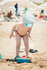 Funny baby in summer cap plays with toys on sandy beach.