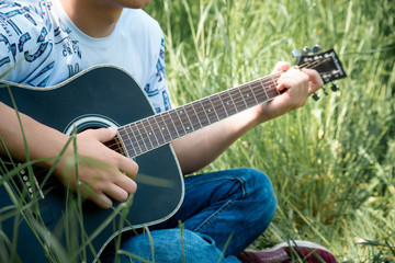 A guy playing a guitar sitting in green grass is a close-up of his hands with a guitar