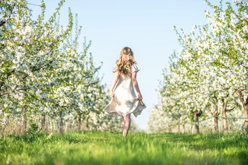 Obraz premium Woman in a blooming orchard at springtime. Enjoying sunny warm day. Retro style dress. Colorful spring moods