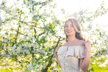 Fototapeta na wymiar Woman in a blooming orchard at springtime. Enjoying sunny warm day. Retro style dress. Colorful spring moods