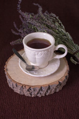  A beautiful cup with fine tea stands on a cut of a tree, on a brown background and on a background of a bouquet of flowers.