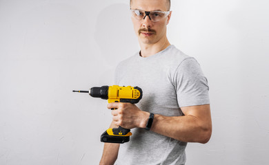 Construction: A man in protective glasses is holding a yellow electric screwdriver.