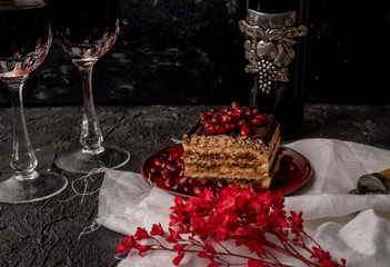 Fototapeta na wymiar sweet, tempting tiramisu, sprinkled with red grains of pomegranate, on a black stone table, next to it red wine in crystal glasses