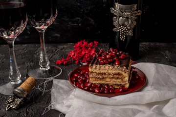 sweet, tempting tiramisu, sprinkled with red grains of pomegranate, on a black stone table, next to it red wine in crystal glasses