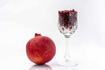 on a white background, isolated, blood-red, pomegranate fruit next to a crystal glass, filled to the brim with fresh, red pomegranate seeds