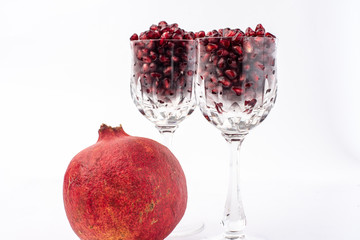on a white background, isolated, blood-red, pomegranate fruit next to a crystal glass, filled to the brim with fresh, red pomegranate seeds