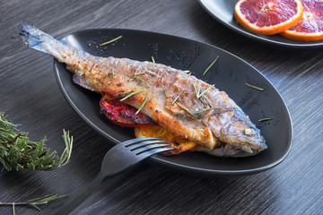 Trout with grapefruit and rosemary fried in a pan on a black tray.