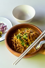 The northen thai dish  khoa soi with fried egg noodles and chopsticks in a clay pot and some garnish in the background, Thailand