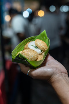 Kanom Krok, the typical thai coconut pancake wrapped in some banana leaves in the hand of a woman on the night market in Chiang Mai, Thailand